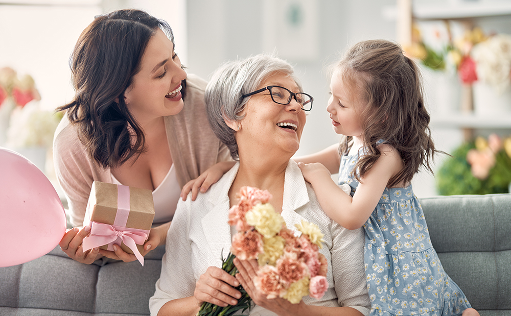 Happy mother’s day Happy mother's day! Child daughter is congratulating mom and granny giving them flowers and gift. Grandma, mum and girl smiling and hugging. Family holiday and togetherness.