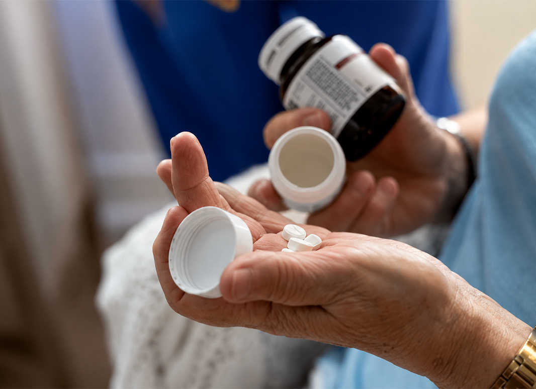 Close-up of a caregiver pouring medication from a pill bottle into a senior resident's hand