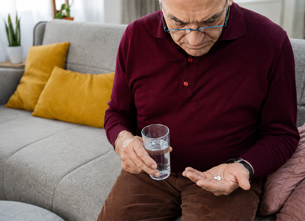 Senior man sorting his daily medication with a glass of water while sitting on a couch