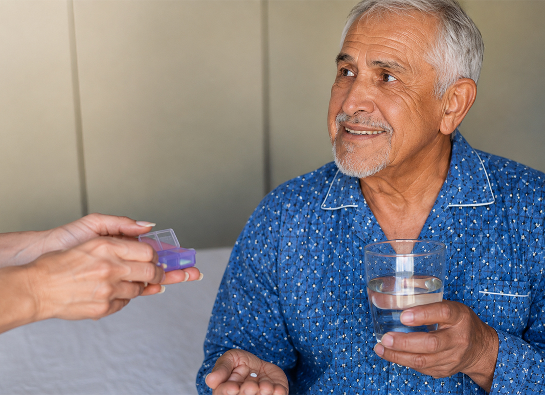 Caregiver handing a pill organizer to a senior man holding a glass of water